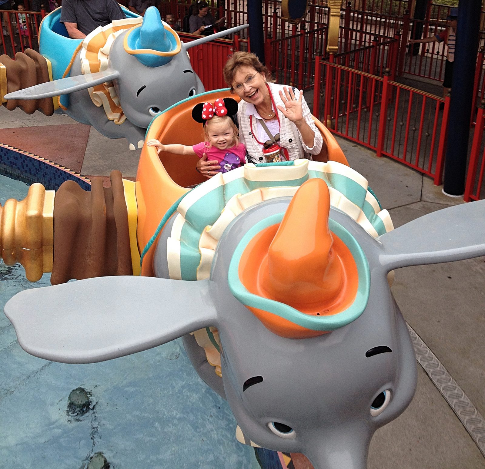 little girl and grandmother smile and wave from dumbo ride