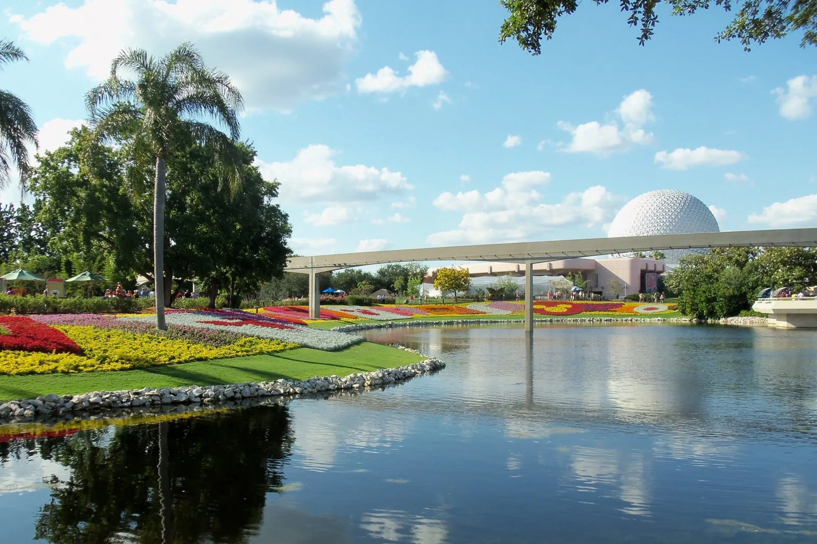 view outside of epcot, colorful flowers, water way, monorail track, and the iconic spaceship earth ride in Epcot