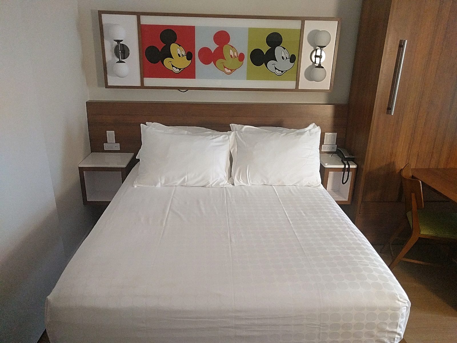 white bed with mickey mouse themed wall decor above