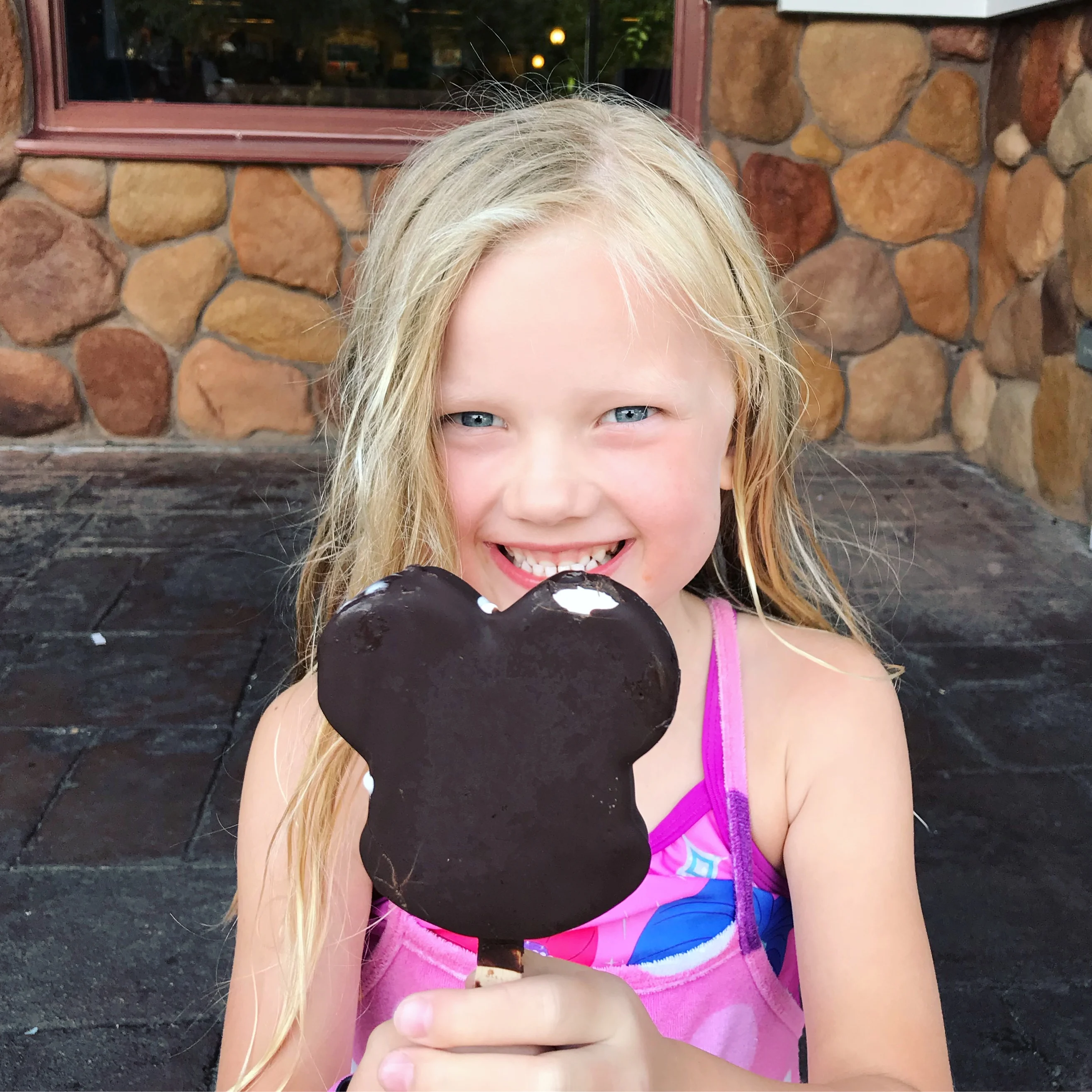 little girl enjoying a chocolate dipped mickey ice cream